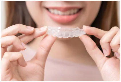 Hands holding a clear orthodontic aligner near teeth